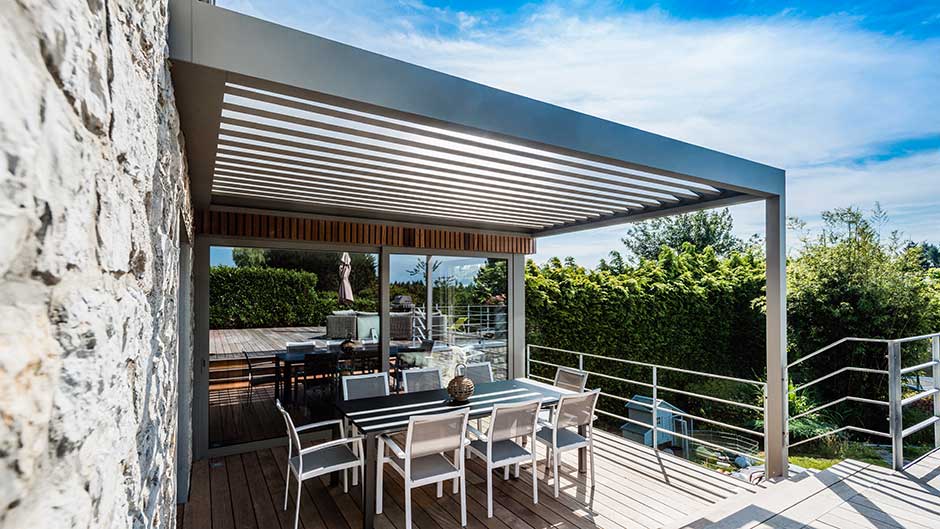 Moderne Terrassenüberdachung mit Esstisch und Stühlen auf Holzterrasse bei Sonnenschein