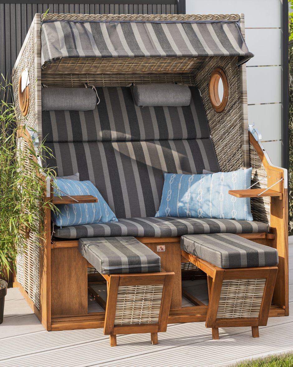Strandkorb aus Holz und Korbgeflecht mit grauer Polsterung auf einer Gartenterrasse