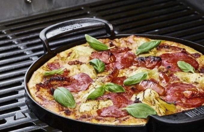 Pizza mit Salami und Basilikumblättern in einer Grillpfanne auf dem Grillrost