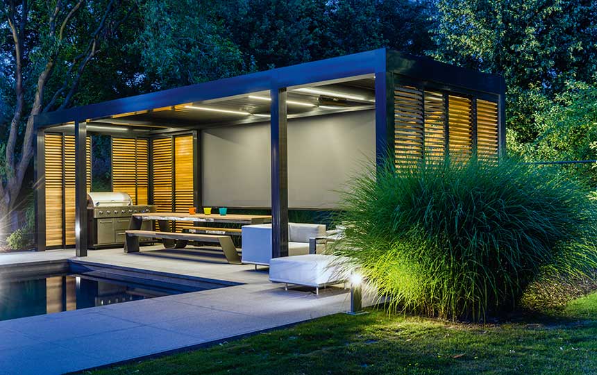 Moderne überdachte Aluminium-Terrasse am Abend, mit Lounge-Möbeln und Grillbereich