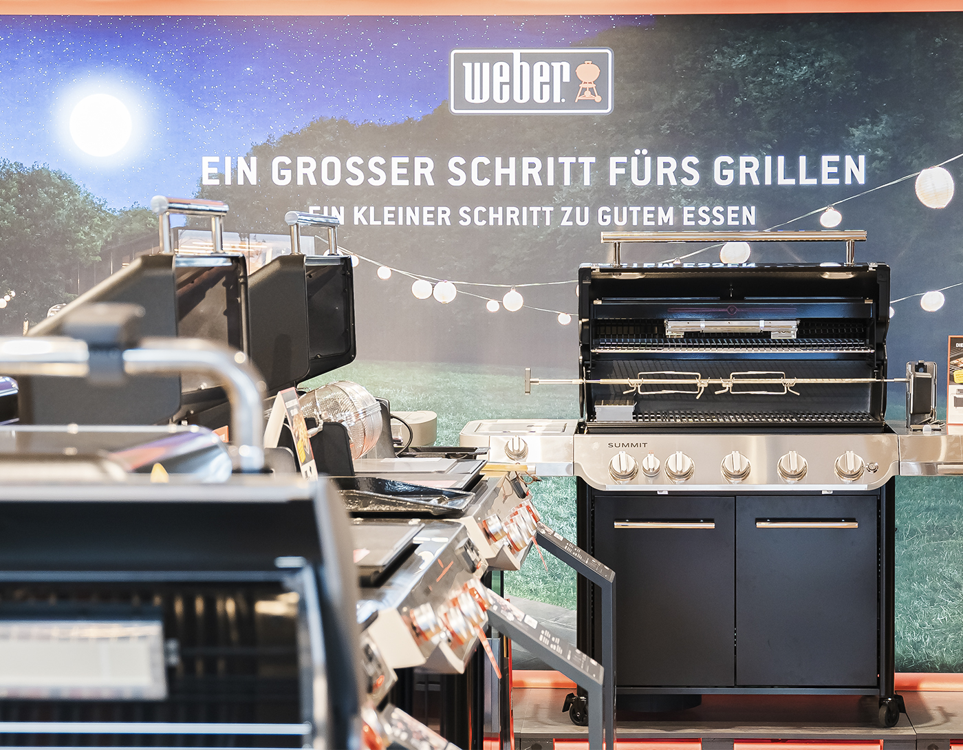 Grill-Ausstellung mit Weber-Gasgrills vor Werbewand mit Schriftzug und Lichterkette