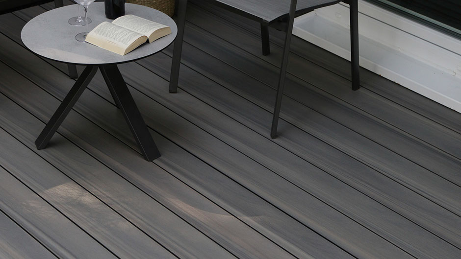 Dunkle HPL-Terrassendielen mit Tisch, Stühlen und Buch im Außenbereich